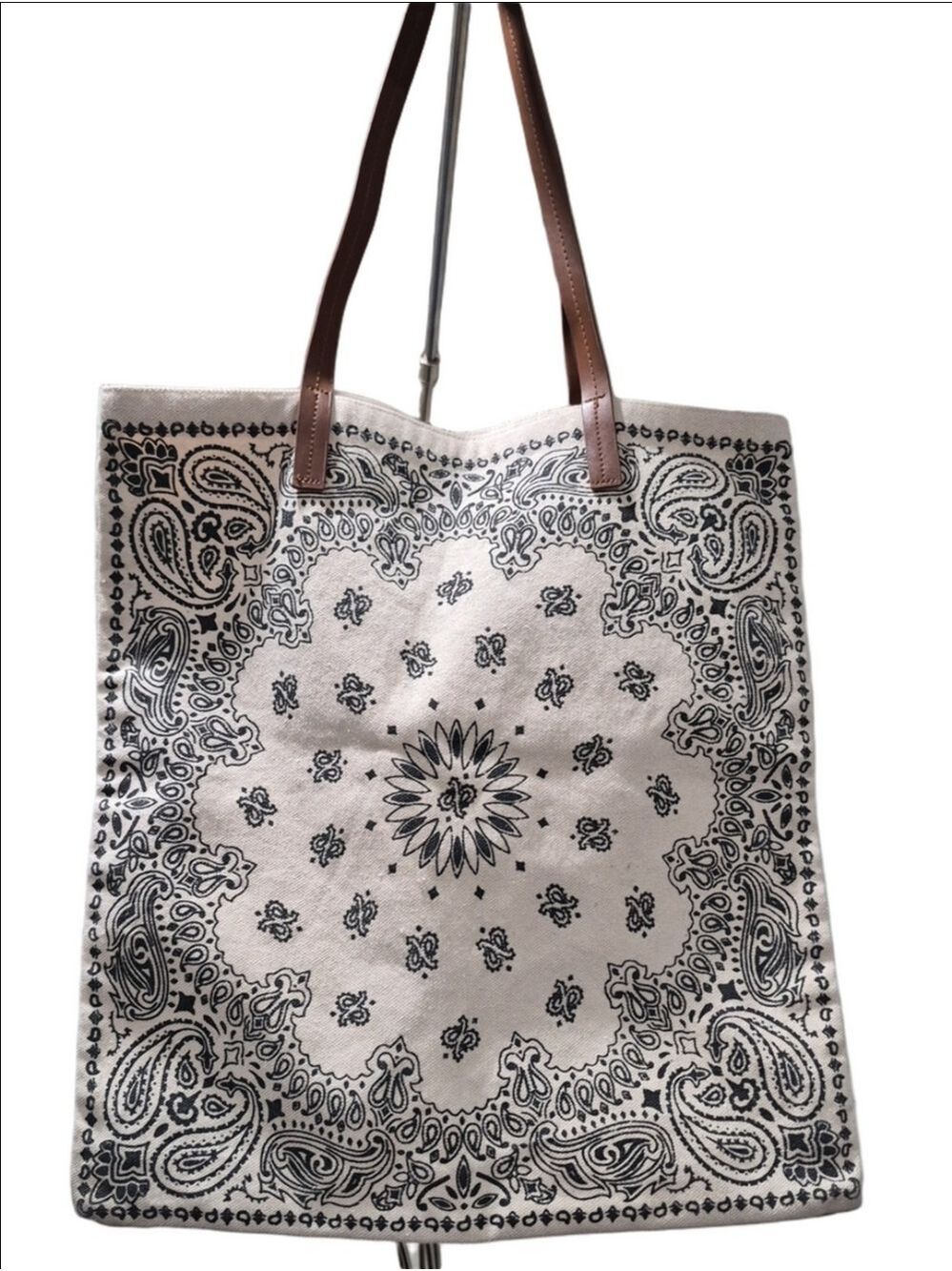 Beige canvas tote bag features a black paisley bandana pattern and brown straps
